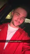 In this selfie-style clip, Kenneth sits inside a car, looking directly at the camera. He is wearing a red jacket over a white t-shirt and has visible facial hair and ear piercings. A Snapchat text overlay reads '2 classes taught today!' as he shares a moment after his teaching day. by @ken_sutton23 with original sound