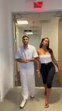 A man and woman walk together down a modern office hallway. The man, identified as Jeremiah Brown, wears an all-white outfit. The woman wears a white crop top and black pants. They smile and gesture towards the camera as they approach, creating a dynamic and engaging entrance. by @findjeremiah with Original Sound by Contains: Right Above It (Edited) - Lil Wayne, Drake