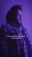 A man with curly hair performs passionately under purple lighting in a teaser for the song 'Wrong Time of Day' by AMH Band. He sings lyrics like 'I keep repeating the words that you said' and 'It's the wrong time of day,' building anticipation before revealing the release date. by @amhbande with amhbande by Original Sound