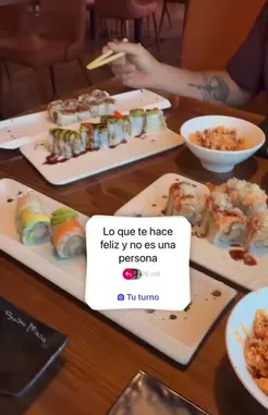 A close-up view of a delicious sushi meal shared by Kastiela Garcia. The camera pans across various rolls, including California rolls and others drizzled with sauce, set on a wooden table. A Snapchat story overlay reads 'Lo que te hace feliz y no es una persona' (What makes you happy and it's not a person), suggesting a theme of finding joy in simple pleasures like food and company. by @kastielagarcia with kastielagarcia by Original Sound
