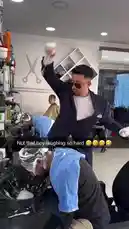 In a bustling barbershop, a barber in a black suit accidentally knocks over a large bowl filled with white foam while washing a client's hair. The foam splatters everywhere, covering the floor, chairs, and another unsuspecting customer sitting nearby. The moment captures a hilarious and messy mishap during a routine haircut. by @eirakoze64 with Original Sound by ogjjoseph
