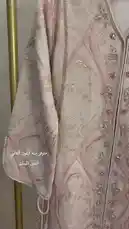 A stunning light pink kaftan dress with intricate silver embroidery and beading is displayed on a mannequin. The camera pans down the garment, showcasing its V-neckline, flowing wide sleeves, and detailed embellishments along the front placket. At the bottom of the frame, a pair of brown heeled sandals rests on the floor, suggesting a complete outfit. by @needle_t with original sound