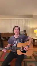 A young musician sits center stage playing an acoustic guitar while his bandmates energetically perform behind him. One member stands over his shoulder, another leans in from the side, and a third joins from the back, all singing passionately into the camera. Their coordinated performance creates a dynamic and intimate live music experience. by @amhbande with amhbande by Original Sound