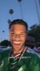 In this energetic clip, creator Jeremiah Brown, wearing a green jersey and multiple silver chains, films himself outdoors at dusk with palm trees in the background. He smiles and laughs while holding up a white cloth and reacting to the text overlay 'WHO'S A CURSE???'. The audio features him shouting excitedly, 'Finally! I've been trying to catch you boys all day!' This short-form content captures a moment of playful fan interaction. by @findjeremiah with Original Sound by findjeremiah