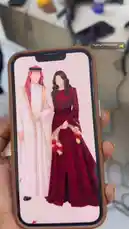 A close-up shot displays a smartphone screen held in hand. On the screen is a digital illustration of a couple in traditional Saudi attire. The man wears a white thobe and red-and-white checkered ghutra, while the woman is in a long, elegant maroon abaya. This image serves as a visual reference for bridal fashion and traditional clothing styles. by @batoolmakeup1 with السعادة والحب في صورة : by ❤️