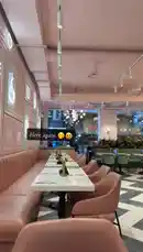This stylish video tour showcases the interior of a trendy café or restaurant, featuring modern decor with pink and white tones, elegant pendant lighting, and a striking black-and-white checkered floor. A long white table is set for guests, while green velvet booths offer cozy seating. In the background, a decorative pink scooter adds a playful touch to the sophisticated ambiance. The space is filled with lush plants and contemporary art, creating a vibrant yet relaxing atmosphere perfect for social gatherings. by @miji-bello with Feel Good by Clara La San