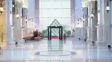 This video documents the launch event for Shams Perfumes, beginning inside a grand, marble-floored hall with a striking glass pyramid centerpiece. A woman in a black abaya and hijab serves as the host, presenting information about the event's schedule, which runs from March 11th to 13th. The video transitions to an outdoor plaza setting before concluding with a screen displaying logos of key partners, including the Ministry of Culture, Awaj Academy, Alhazaa, Y.E.C., and Qatar Voluntary. The overall tone is one of elegance and cultural significance. by @shamslinep with shamslinep by Original Sound