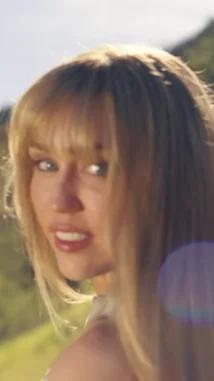 A dynamic visual journey through Miley Cyrus's career, showcasing her transformation from a young star to a global icon. The montage features candid moments, including her in a blue cardigan, embracing her roots in a denim vest, and her signature blonde hair flowing in the sun. It captures her in various iconic settings, from the Hollywood Hills to urban streets, highlighting her fashion evolution and charismatic presence. by @mileycyrus with Original Sound by Contains: Younger You (From the "Hannah Montana 20th Anniversary Special") - Miley Cyrus, Lainey Wilson
