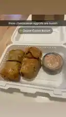 In this quick foodie snapshot, we see a close-up of crispy, golden-brown cheesesteak egg rolls served with a side of dipping sauce in a takeout container. The text overlay reads 'these cheesesteak eggrolls are bussin' and tags the location as 'Ocean Casino Resort.' This enticing treat highlights a popular fusion snack enjoyed at the resort. by @dimpled.diva02 with original sound