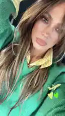 Jennifer Lopez takes a selfie during her travels, showcasing her stylish look with a green sweater layered over a yellow collared shirt. The image features playful airplane and heart stickers, suggesting she is on a flight. This candid moment captures her effortless chic style. by @jlobts with Original Sound by Contains: Nicole Kidman - ADÉLA