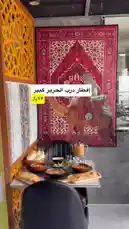 A beautifully set table awaits at مطعم درب الحرير, showcasing traditional flatbreads, fresh salads, and warm bread rolls. The restaurant's decor, featuring intricate red tapestries and ornate wooden screens, creates an inviting atmosphere for a genuine culinary journey. by @darbalhareer with Original Sound by darbalhareer