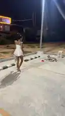 In a quiet, dimly lit parking area at night, a woman in a white dress approaches a stray dog resting on the pavement. She gently bends down to interact with the animal, showing care and compassion. A red bowl sits nearby, suggesting she may be feeding or offering water. The scene captures a peaceful and touching moment of human-animal connection. by @tinybenzy1 with Original Sound by tinybenzy1