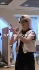 A woman with blonde hair and glasses, identified as SPECS, speaks passionately about technology's role in enhancing humanity. She gestures while wearing futuristic-looking glasses, emphasizing her point that technology should 'help you feel more human' and 'build systems that genuinely help people.' A man in the background holds a long, curved black object, possibly a prop or piece of tech. by @specs with Original Sound by specs