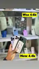 A hand holds three different iPhone models side-by-side, showcasing their camera systems. On-screen text highlights a price reduction from 'Was 4.6k' to 'Now 4.4k'. The background features a retail display with more phones, suggesting a store environment. This visual strongly implies a sales event or clearance, making it highly relevant for users searching for deals. by @ab_god18 with original sound