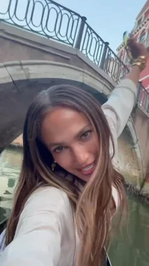 Jennifer Lopez shares a scenic moment on a gondola in Venice, Italy. She smiles and poses for the camera while gliding through the canals under a stone bridge, capturing the romantic atmosphere of her vacation. by @jlobts with Original Sound by Contains: Like a Virgin (2024 Remaster) - Madonna