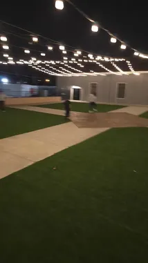 This nighttime scene captures a lively outdoor gathering under a canopy of string lights. Several people are seen enjoying various activities on a grassy area with concrete walkways. The atmosphere suggests a casual party or social event, possibly hosted by Maksim Kochkin. by @kochkinmax with kochkinmax by Original Sound