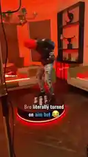 In a room bathed in vibrant orange light, a person wearing a black puffer jacket, ripped jeans, and a red beanie performs an energetic and slightly chaotic dance on a circular platform with glowing red edges. The dance moves are exaggerated and frantic, creating a humorous effect. Text overlay reads 'Bro literally turned on aim bot 😂', suggesting the dance is so wild it looks like it's being controlled by a robot. A male voice can be heard speaking in the background. by @uk-gos with Original Sound by uk-gos