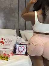 In this stylish and intimate scene, Big Erima 💅🏾 is seen showcasing her trendy pink shorts and white crop top while interacting with a tablet displaying a Valentine's Day-themed heart graphic. A beautifully arranged 'Valentine's Curve Box' from Erima sits nearby, suggesting a special gift reveal or themed content. The setting is a cozy bedroom with soft lighting, creating a romantic and personal atmosphere perfect for celebrating love and self-expression. by @eboggar1 with original sound