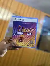 A close-up showcase of the NBA 2K24 physical game case for PlayStation 5, held in hand against a warm-toned background. The cover art features a dynamic basketball player in mid-action, highlighting the game's release and visual appeal. by @frekasglobal with original sound