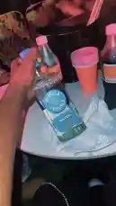 A close-up shot captures a hand holding a bottle of Omeca Silver Tequila at a lively party. The table is set with orange cups, another bottle, and a napkin, all under vibrant red lighting. The scene evokes a fun, social atmosphere perfect for celebrations. by @big20247443 with CHICKEN RAP 🤣 by NAIJAEVERYTHING