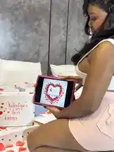 In a stylish bedroom setting, Big Erima showcases a Valentine's Curve Box while interacting with a tablet displaying a custom heart-themed digital message. This scene blends romance, technology, and personal branding, demonstrating a modern approach to celebrating special occasions. by @eboggar1 with original sound