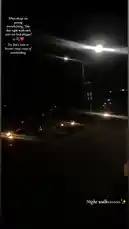 This nighttime scene captures a quiet urban street illuminated by bright overhead streetlights. Parked cars line one side of the road, their headlights off, while the dark sky and surrounding shadows create a moody atmosphere. The camera remains mostly static, focusing on the contrast between light and darkness, showcasing typical city night life. by @justt_dhammie with 🥹-😔 by Mr.jayce 🧟‍♂️