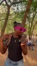 In a sun-dappled park setting, content creator Bene Sassy confidently handles a large python. She smiles at the camera while showcasing her pet snake draped over her shoulders and held in her hands, creating a striking and memorable moment. by @be-sassyish with original sound