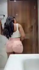 In this short clip, Big Erima is seen from behind in a bathroom setting, showcasing her outfit. She adjusts her long, dark hair while wearing a white crop top and tight-fitting pink shorts with prominent back pockets. The scene captures a candid moment of personal style and presentation. by @eboggar1 with Original Sound by eboggar1