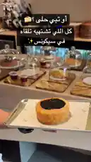 A close-up view of a golden-brown pastry filled with rich chocolate ganache, presented on a branded paper liner atop a metal tray. The setting is a modern café counter with other desserts displayed under glass domes, suggesting a high-quality bakery experience. by @sequence-coffee with موسيقى رايقه 🎵 by موسيقى
