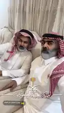This static image captures two Saudi men dressed in traditional thobes and ghutras, seated together indoors. Their attire highlights cultural heritage and national identity. A watermark featuring Arabic script and a palm tree logo suggests the image may be part of a social media post celebrating Saudi culture. by @tr3i5 with عانو ذا الشايب الي قهرهم by .