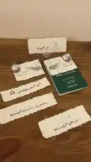 This video showcases a beautifully arranged display of personalized wedding invitation cards and keepsakes laid out on a wooden surface. The items feature elegant Arabic calligraphy, English text, and symbolic imagery such as wings and hearts, creating a romantic and culturally rich presentation. One card prominently displays 'Abd & Wael, 9 July 2026,' indicating a future wedding date. Another card reads 'مرحبا' (Welcome), while others contain heartfelt messages like 'أحبك' (I love you) and 'نرحب بكم في حفل زفافنا' (We welcome you to our wedding). A green Kingdom of Saudi Arabia passport is placed among the invitations, adding a unique touch. The overall aesthetic suggests a modern, bilingual celebration blending tradition with contemporary design. by @r200an with original sound