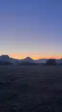 A breathtaking view of a mountain range silhouetted against a vibrant sunset sky. The camera pans slowly across a vast, open field, capturing the tranquil beauty of nature at dusk. This peaceful landscape offers a moment of calm and reflection. by @itzz.angyy with original sound