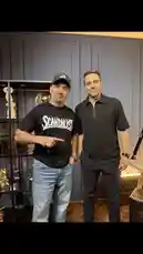 In this exclusive behind-the-scenes look from Code Behind Success, two individuals share a moment in a stylishly modern room. One man wears a 'SCANDALOUS' t-shirt and a baseball cap, pointing towards the camera with a confident gesture, while his companion stands beside him in a black polo shirt. The setting features contemporary decor, including a display shelf with various items, suggesting a casual yet professional atmosphere. This candid interaction hints at a deeper story or collaboration, inviting viewers into a world where success meets personal style. by @codebehindsucce with original sound