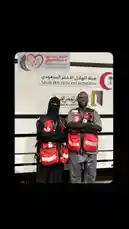Two volunteers from the Saudi Red Crescent Authority stand proudly in front of their mission vehicle. Dressed in official red vests and traditional attire, they represent the organization's commitment to humanitarian service and peace messaging. by @peace.message with original sound