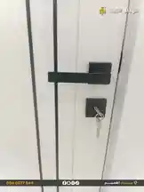 A close-up view of a sleek, modern black door handle installed on a white door. A key is inserted into the lock below the handle, showcasing a clean and contemporary design ideal for residential or commercial properties. This product is offered by الهيكل الثابت للمقاولات. by @fixedstructure with original sound
