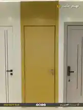 A static showcase of three contemporary interior door styles presented by الهيكل الثابت للمقاولات. The central door features a warm wood-grain finish, flanked by a sleek white door with black vertical lines on the left and a light gray textured door with a black handle on the right. This display highlights design options for modern homes and commercial spaces. by @fixedstructure with original sound