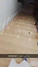 This walkthrough video shows the final stages of a staircase renovation project. It features newly installed light-colored wood-effect waterproof SPC flooring covering every step, secured with yellow tape during installation. White decorative riser panels have been added along the wall, and a sleek black metal railing has been fitted. A hand points to the work, highlighting the clean finish and modern aesthetic achieved with these materials. by @zoodasas with Original Sound by zoodasas
