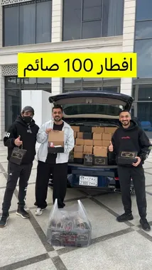 في مشهد يجمع بين العمل الخيري والتنظيم المتقن، يظهر الدحومي999 مع فريقه وسط سيارة مفتوحة الباب محملة بعلب الطعام. يرتدي الفريق ملابس رياضية سوداء ويحملون صناديق توزيع، بينما يقف أحدهم يُظهر صندوقًا للإمساك به. يبرز في الصورة لافتة كبيرة باللون الأصفر تحمل عبارة 'افطار 100 صائم'، مما يشير إلى حملة إغاثية لدعم الصائمين. يعكس المشهد جوًا من التعاون والمسؤولية المجتمعية، ويُظهر التحضير الجيد للحملة الخيرية. by @d7oomysnap with original sound