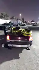 In this nighttime scene, M showcases his customized dark red Chevrolet Camaro SS. The car features a prominent dual exhaust system and is loaded with two large, custom-wrapped wheels on its trunk. The setting appears to be a private lot or garage area, illuminated by overhead lights, suggesting a moment of preparation or display before a night out. by @mo_kbs8 with 😣😣🔊. by sC: Lj-wa