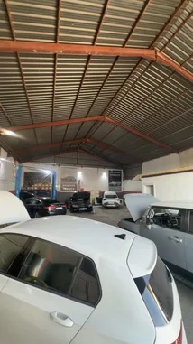 This time-lapse footage captures the bustling activity inside a professional auto repair garage. Multiple vehicles, including white and black sedans, are seen undergoing maintenance with hoods open under bright work lights. A large hydraulic lift stands ready in the background, while mechanics move about efficiently. The industrial space features a high, corrugated metal roof supported by red beams, highlighting the practical setup of a modern service center. by @hawkar_service with original sound