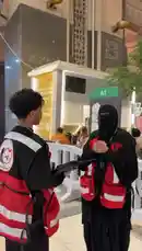 This video shows members of the فريق رسالة سلام التطوعي (Message of Peace Volunteer Team) providing first aid during a nighttime event. A female volunteer administers an automated external defibrillator (AED) to a person lying down while another volunteer observes. The team, identifiable by their red vests, is seen managing the situation calmly and professionally. by @peace.message with Original Sound by peace.message