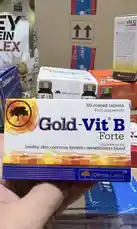 A close-up shot reveals a hand holding a box of Gold-Vit B Forte, a food supplement from Olymp Labs. The packaging highlights benefits for healthy skin, nervous system, metabolism, and blood. In the background, other health products like collagen and protein powder are visible, suggesting a focus on wellness and nutrition. This scene is ideal for triggering a deeper crawl due to its clear product focus and context. by @lanutritioniraq with original sound