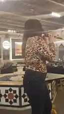 A woman sings passionately into a microphone while walking around a stylish lounge or restaurant. She wears a leopard print top and jeans, performing for a few seated guests. The venue features modern decor with geometric tile patterns, chandeliers, and large screens displaying cityscapes. by @mo.fouadziko with Original Sound by mo.fouadziko