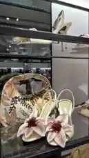 A close-up showcase of luxury women's accessories, featuring intricately beaded floral heels and a matching embroidered handbag. The display highlights detailed craftsmanship and modern fashion design, set within a stylish retail environment. by @ru.ab71 with original sound