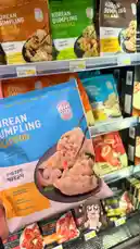 A shopper browses the frozen food aisle, highlighting various Korean dumpling brands like 'Korean Dumpling' and 'Korean Dumpling Seafood'. The focus shifts to a close-up of the seafood dumpling package, showcasing its shrimp filling. An animated avatar appears, suggesting a review or taste test is about to begin. by @ab.7955 with original sound