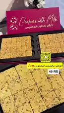 This video showcases a beautifully presented box of 'Cookies with Milk' from the brand 'براون تشوكليت'. The golden-brown cookies are neatly arranged in a black tray and displayed alongside their vibrant pink packaging. A Snapchat QR code and a price tag of '49 RS' are visible, suggesting a promotional product. The scene is styled with white flowers in the background, creating an elegant and appetizing presentation perfect for food enthusiasts and dessert lovers. by @ch11.30 with original sound
