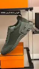 A close-up view of a modern men's sneaker showcased on an orange box within a high-end retail environment. The shoe features a mesh upper, sleek design, and distinctive striped sole. Arabic text on screen indicates pricing information, suggesting a commercial product display. by @lussowatches with original sound