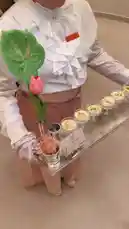 A server in a white ruffled blouse and pink skirt gracefully carries a silver tray laden with small glasses of creamy dessert garnished with pistachios. A vibrant green lotus flower and a pink tulip add a touch of color to the elegant presentation. by @moneeragh with ايسكريم ايسكريم 🕺🕺 by Vip.fj