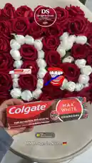 A hand holds a box of Colgate Max White Charcoal toothpaste in front of a large, circular arrangement of red and white roses. The 'DS Drogerie Store' logo is visible multiple times on screen. A sticker of a smiling mouth with a toothbrush is placed on the bouquet. An audio jingle for 'DS Drogerie' plays throughout the clip. by @dsdrogeriestore with DS🇩🇪 by DS drogerie store🇩🇪