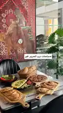 This video showcases a beautifully arranged table at مطعم درب الحرير, featuring traditional dishes such as freshly baked flatbreads, savory pies, and a hearty meat dish served on wooden boards. The setting includes elegant decor with a striking red carpet design and lush green plants, creating an inviting atmosphere. A text overlay highlights 'صباحات درب الحرير غير' (Morning at Durb al-Hir), suggesting a special breakfast or morning offering. This visually rich presentation emphasizes cultural authenticity and culinary appeal, enticing viewers to explore the restaurant's offerings. by @darbalhareer with original sound